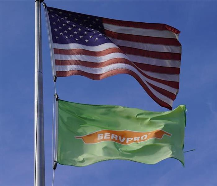 A flag post holds two flags waving in the wind, an American flag and a SERVPRO flag.
